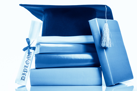 A mortarboard and graduation scroll, tied with red ribbon, on a stack of booksの写真素材
