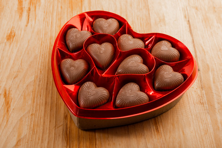 chocolate pralines in red heart shape box on tableの写真素材