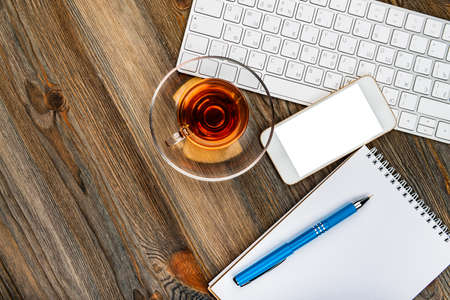office table with computer keyboard, mouse, cup of tea and smartphoneの写真素材