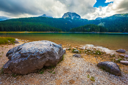 Stone on the background of azure lake and mountain Bobotov Kuk. Black Lake. Durmitor National Park. Montenegro.の写真素材