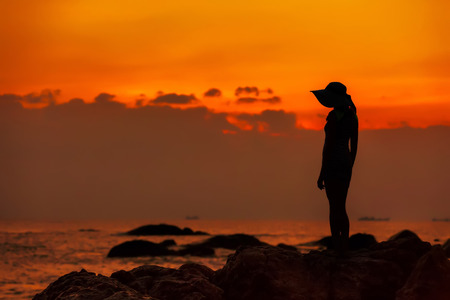Silhouette of a girl in a hat against the background of an orange sea sunset. End of the Earth. Hainan, China.の写真素材