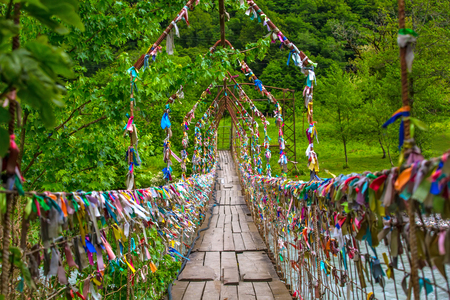 A pedestrian suspension bridge across the river in Abkhazia. Multicolored ribbons are hung on it. Suspension bridge in Abkhazia.の写真素材