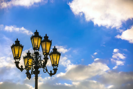 Street black lamppost Pushkin with a lantern made of iron against a background of a sunny blue sky with white clouds. City lamppost, Moscow, Russia.の写真素材