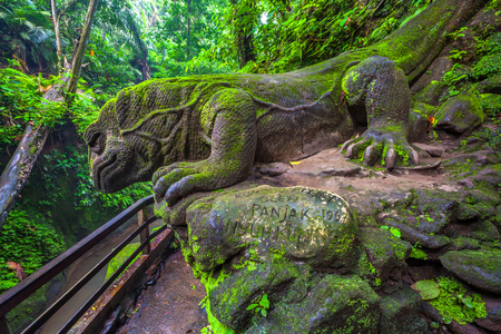A stone statue of the Komodo monitor, covered with moss and lichen in a tropical green forest near...