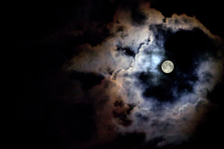 The moon illuminates the black sky. Copy space for text. The moon behind the clouds.の写真素材