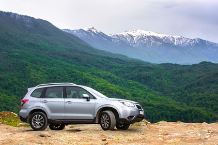Subaru Forester at Sochi, Adler, Russia - May, 2016. A car is a gray SUV on top of a mountain on a background of a green forest on a slope and a snowy peak.のeditorial素材
