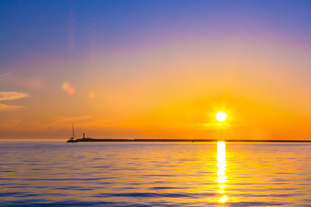 Summer bright orange sunset with clouds in the sky and silhouette of a lighthouse on the shore. Coastal seascape on the Black Sea, Sochi, Russia.の写真素材