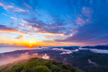 Sunset hidden behind clouds and fog over hills, bright yellow sun on colorful cloudscape, blue violet orange sky. Panorama of the Black Sea coastline from Akhun mountain, Big Sochi, Russia.の写真素材