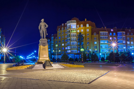 Monument to Great Peter in the darkness of the embankment on backdrop of urban modern residential buildings and walking alley illuminated by light of street lampposts.のeditorial素材