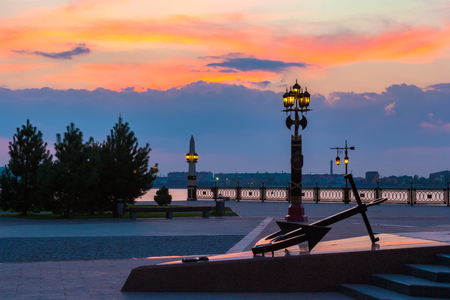 Decorative lamppost with anchor on the square in front of the Volga river bank during sunset with a beautiful colorful sky and an outgoing orange sun.の写真素材