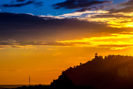 Silhouette of monument to Salawat Yulaev, folk hero on a horse against a bright yellow blue sky with clouds and orange sun disk at city sunset.の写真素材