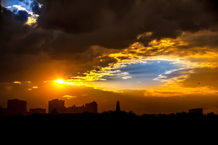 Bright colorful blue sky through yellow rain clouds with a silhouette from the rays of the sun in the evening in the dark at sunset in the city.の写真素材