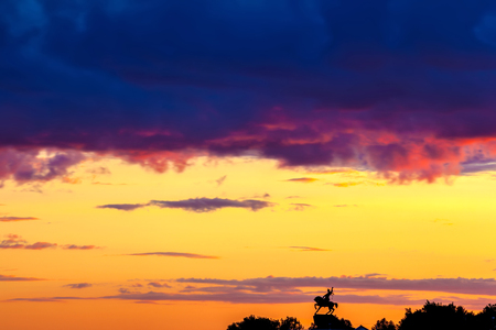 Silhouette of monument to Salawat Yulaev, folk hero on a horse against a bright yellow purple violet sky with clouds and orange sun disk at city sunset.の写真素材