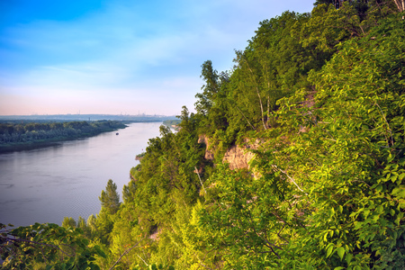 A large cliff overgrown with green grass and trees dominate over the White River in the evening at dusk during sunset under a clear blue sky.の写真素材