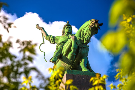 Majestic bronze green monument to Salawat Yulaev, close-up shot through spring foliage on a bright summer day. Folk hero on a horse with whip in his hand.のeditorial素材