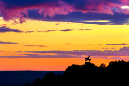 Silhouette of monument to Salawat Yulaev, folk hero on a horse against a bright yellow purple violet sky with clouds and orange sun disk at city sunset.のeditorial素材
