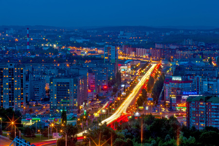 Panorama of the night modern city, the central street in the yellow light trails of passing cars between the sleeping areas in blue twilight color.のeditorial素材
