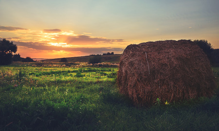 Beautiful summer scene with setting sun and straw bale in the field.Orange sky with clouds over the green meadow.Natural light.の写真素材