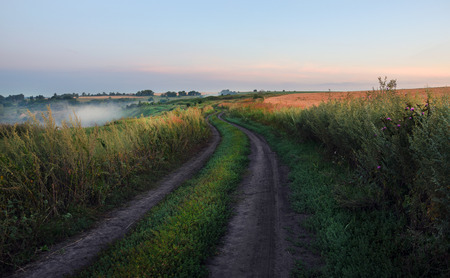 Summer countryside landscape with dirt road.Twilight.Foggy weather.Calm.Tula region, Russia.の写真素材