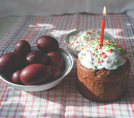 Painted red easter eggs in a bowl and cake with burning candle.Traditional food for the Easter...