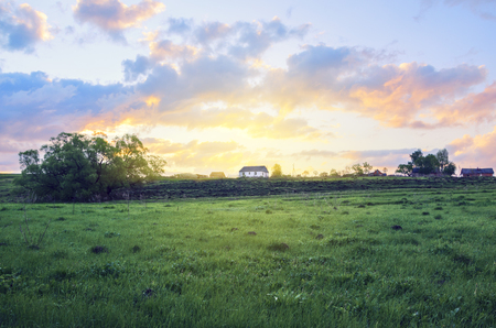 Empty green meadow on a background of country house and rising sun.の写真素材