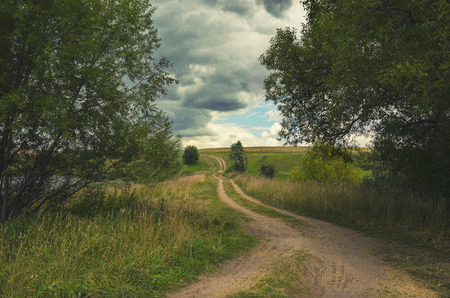 Cloudy summer landscape with road in the sky. Fields, green meadows and woods.