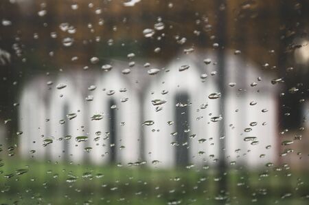 Blurred view of row of white houses through car windshield in rainy autumn morning.