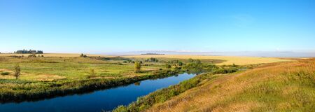 Sunny rural landscape with river and golden fieldsの写真素材