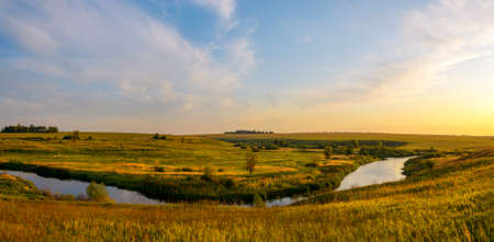 Beautiful panoramic rural nature landscape.Sunny view of small river and green meadows with trees on...