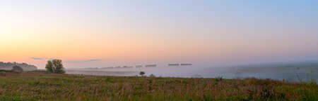 Panoramic view of farm fields and green hills during foggy sunrise.