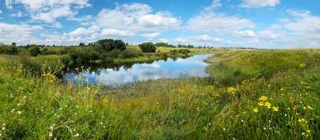 Beautiful landscape with calm river and green hills with trees at sunny summer day.