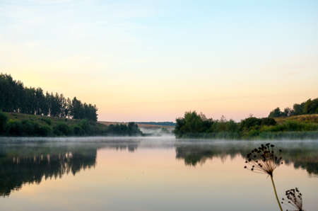 Tranquil landscape with calm lake during foggy sunrise.の写真素材