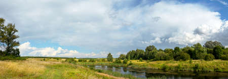 Panoramic summer rural landscape with calm lake and green hills in sunny day.