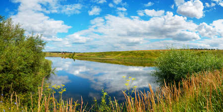 Beautiful panoramic rural landscape with calm river and green hills with trees at sunny summer day.の写真素材