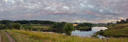 Tranquil summer landscape with river and green hills during cloudy morningの写真素材