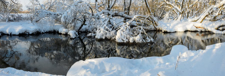Frosty winter scene with forest river on a sunny morning. Beautiful snow covered trees in the glow of rising sun.の写真素材