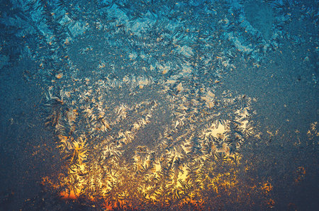 Icy frosty pattern on a window with light of setting sun behind.Winter sunset scene.Christmas background.Abstract rime texture.の写真素材