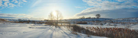 Sunny panoramic early springtime landscape.Beautiful view of frozen river and snow covered fields during sunny march morning.の写真素材
