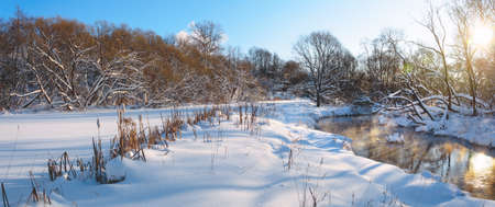 Frosty winter panoramic landscape with snow coverd forest lawn and forest river during sunny january morning.の写真素材