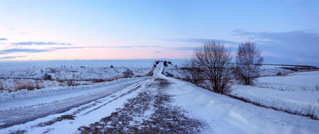 Winter landscape with ground rural road passing through fields at sunriseの写真素材
