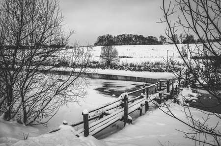 Black and white winter rural landscape with old wooden bridge and calm riverの写真素材
