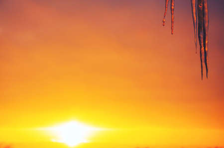 Hanging icicles on a background of setting sun and sunset sky. Selective focus. Springtime or winter scene.の写真素材