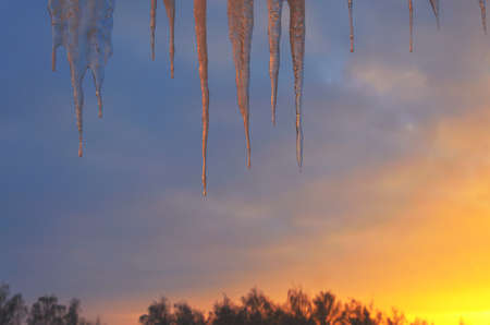 Hanging icicles on a background of setting sun and sunset sky. Selective focus. Springtime or winter scene.の写真素材