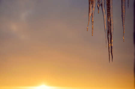 Hanging icicles on a background of setting sun and sunset sky. Selective focus. Springtime or winter scene.の写真素材
