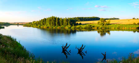 Summer serene landscape with calm river and green hills at sunrise.の写真素材