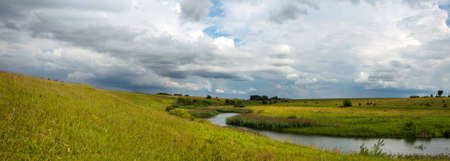 Summer cloudy landscape with dark stormy clouds over the calm river and green meadows.の写真素材