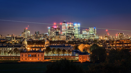London, UK - October 25, 2015: High visible prime meridian beam at night in London Greenwich Park near Queen's House and the Naval College and with the Canary Wharf skyline with its corporate office buildings in the background.のeditorial素材