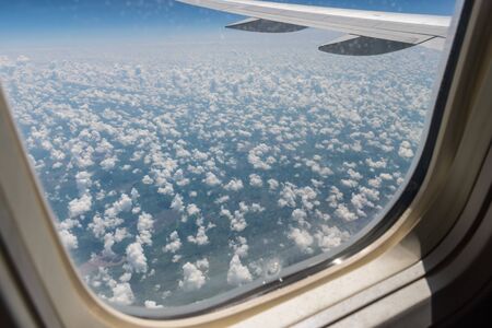 View from the planes porthole on the planes wing, the ground below and the clouds of a summer day in flightの写真素材