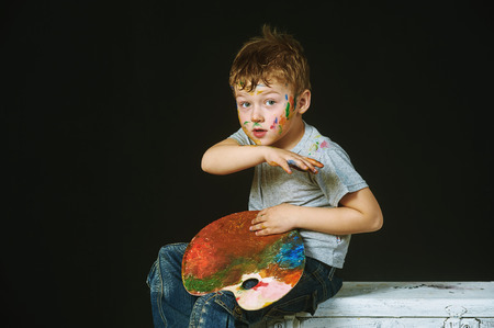 Boy with hands painted in bright colors, with palette in handの写真素材