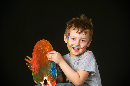 Boy with hands painted in bright colors, with palette in handの写真素材